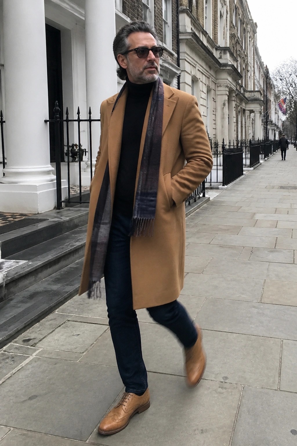 Man in tan overcoat and plaid scarf walking on city sidewalk