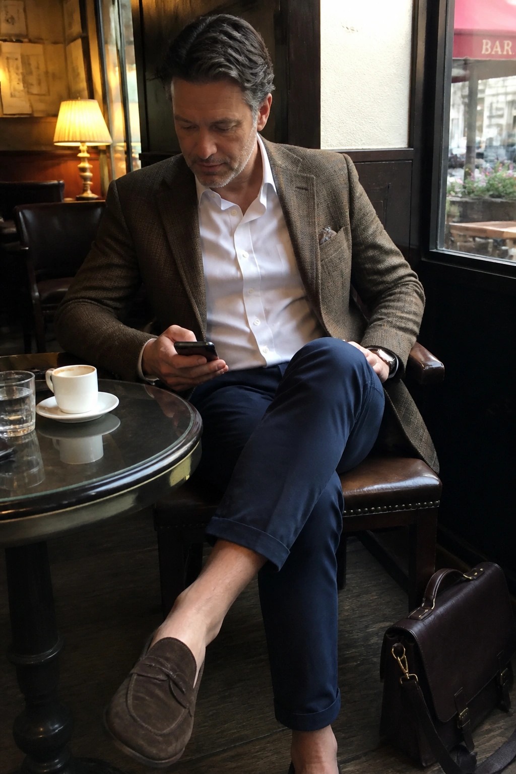 Man in brown tweed jacket checks phone at cafe table with coffee and briefcase