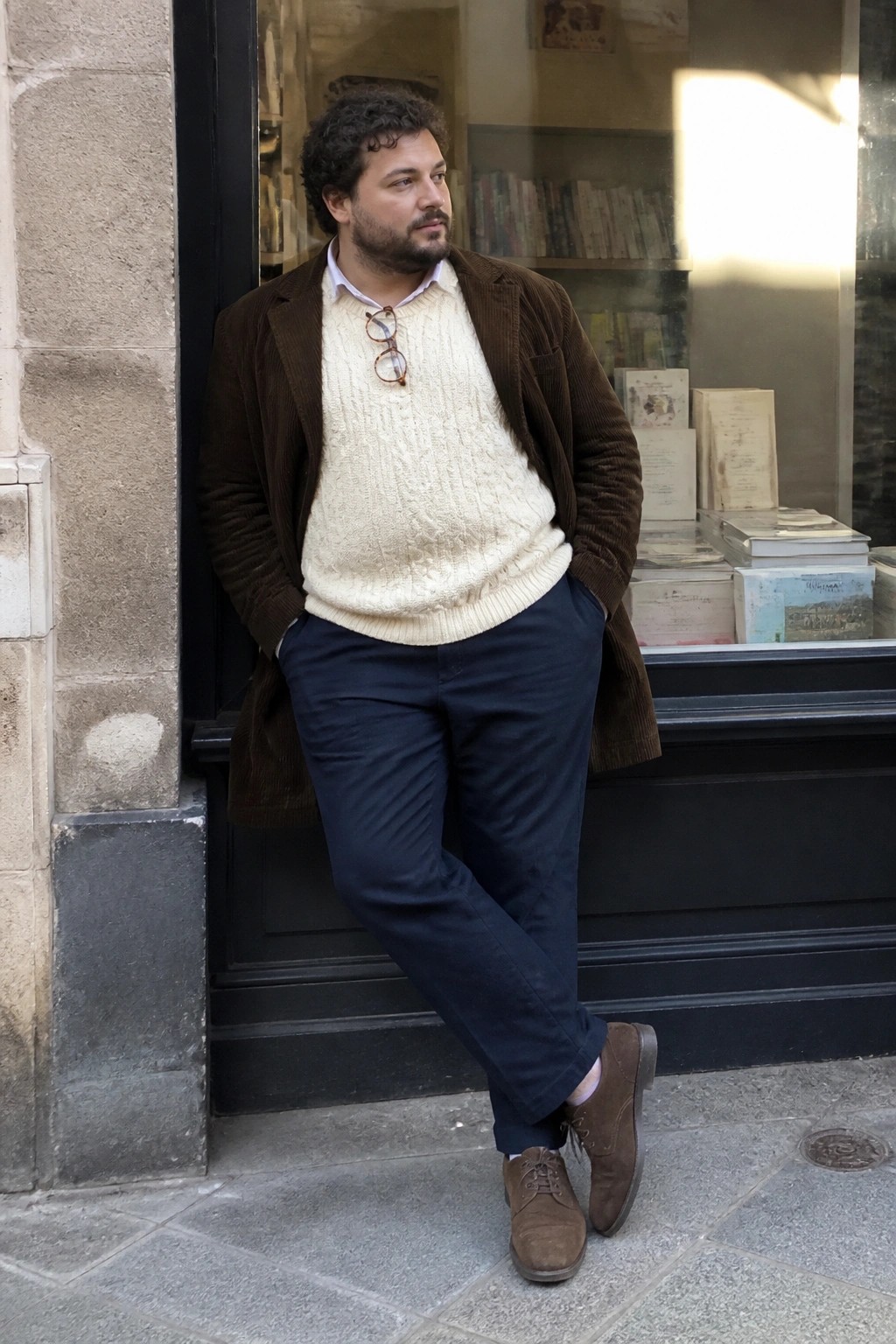 Curly-haired bearded man in brown corduroy jacket and cream sweater by bookstore window