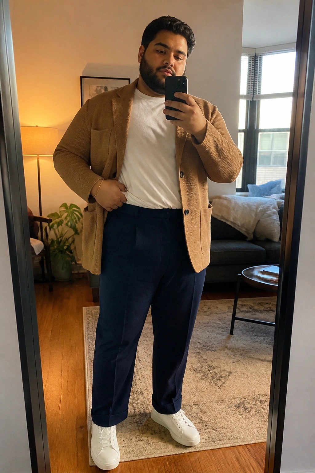 Man in brown corduroy blazer, white t-shirt, navy pants, white sneakers taking mirror selfie