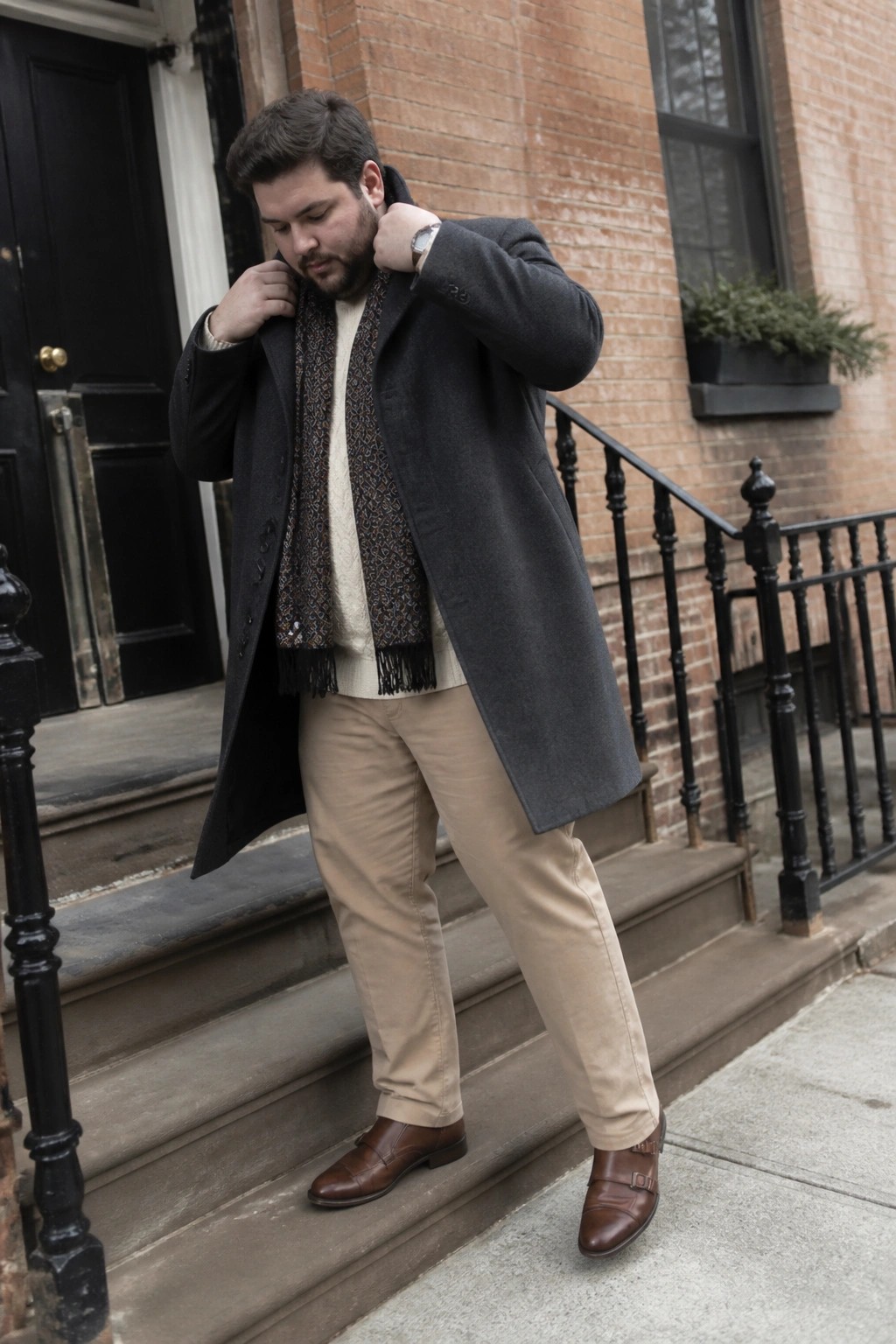 Man in gray overcoat and patterned scarf adjusts collar on stone steps