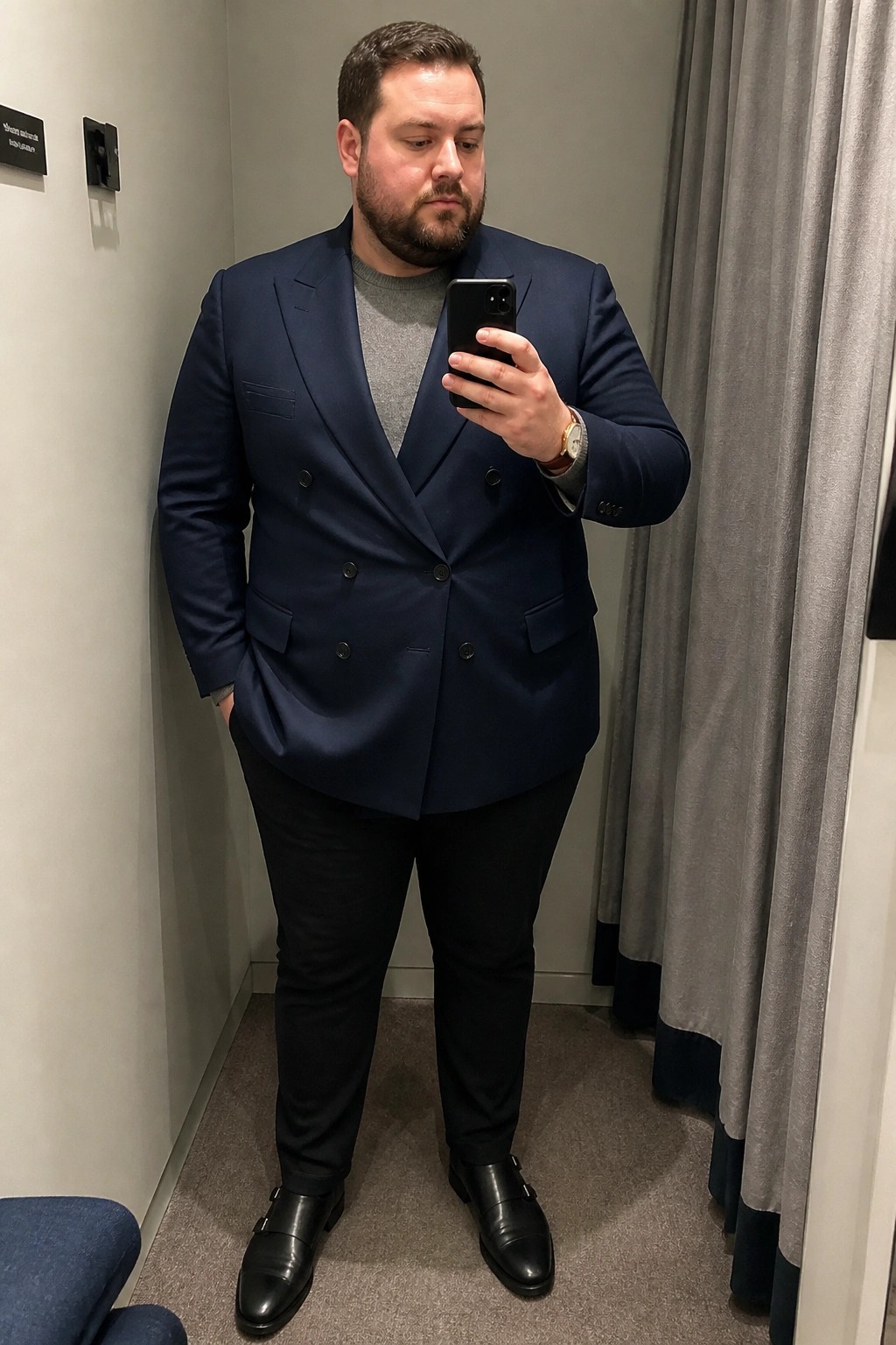 Man in navy double-breasted suit jacket takes mirror selfie in dressing room