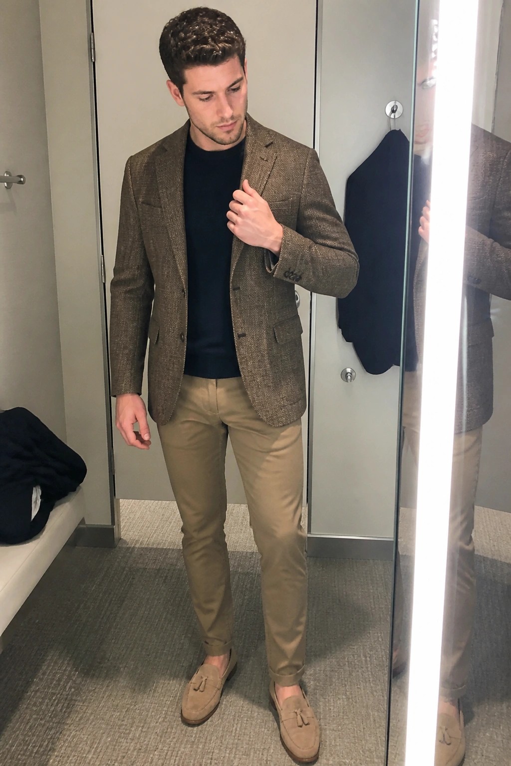 Man wearing brown tweed blazer over navy sweater with khaki pants and beige suede tassel loafers in a fitting room mirror.