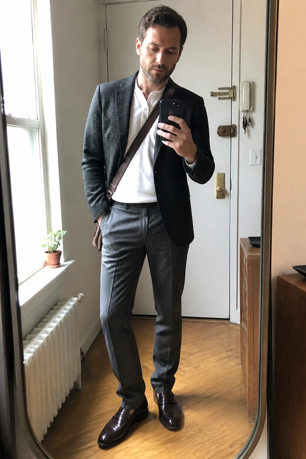 Man in dark textured blazer, white shirt, gray trousers taking mirror selfie.