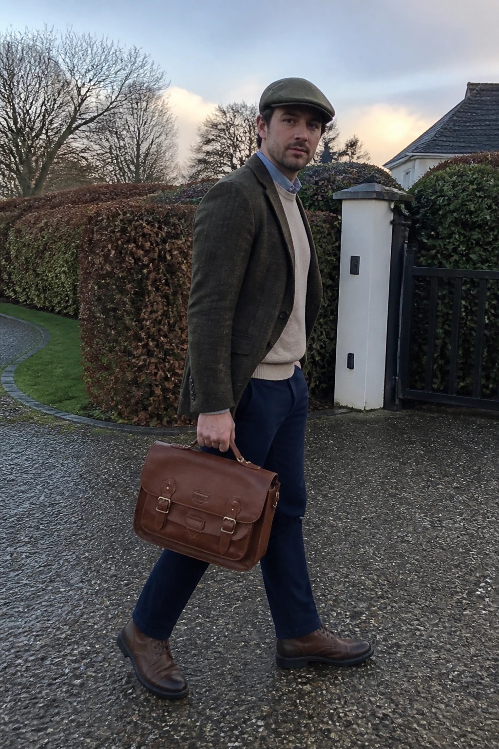 Man in tweed jacket and flat cap carrying leather briefcase on gravel path