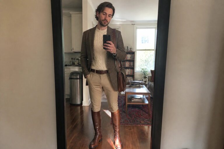 21 Classic Equestrian-Inspired Old Money Fall Outfits for Men Man in brown tweed blazer, cream sweater, tan pants and tall brown boots taking mirror selfie.