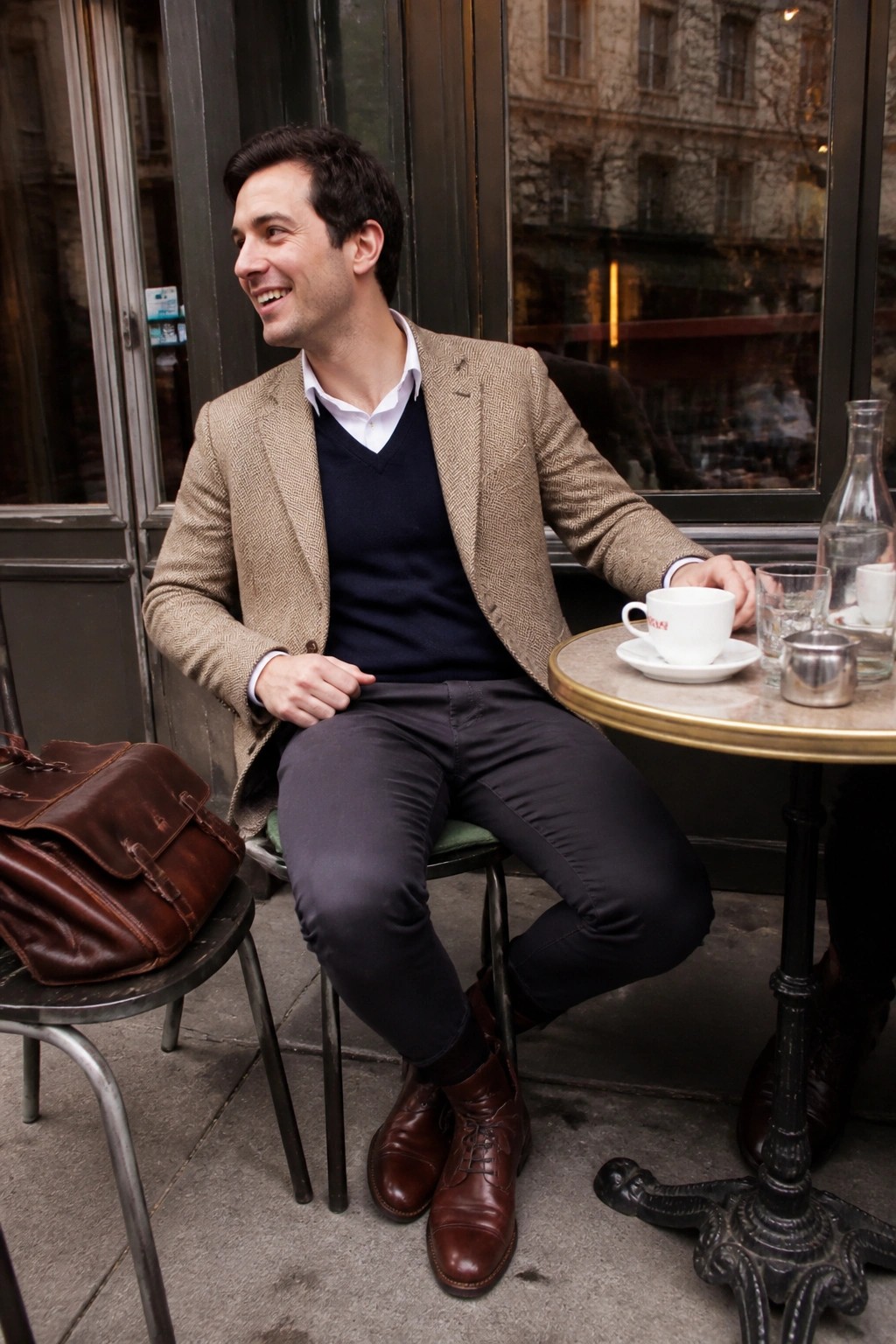 Man in tweed blazer and navy sweater at outdoor cafe with coffee and leather bag