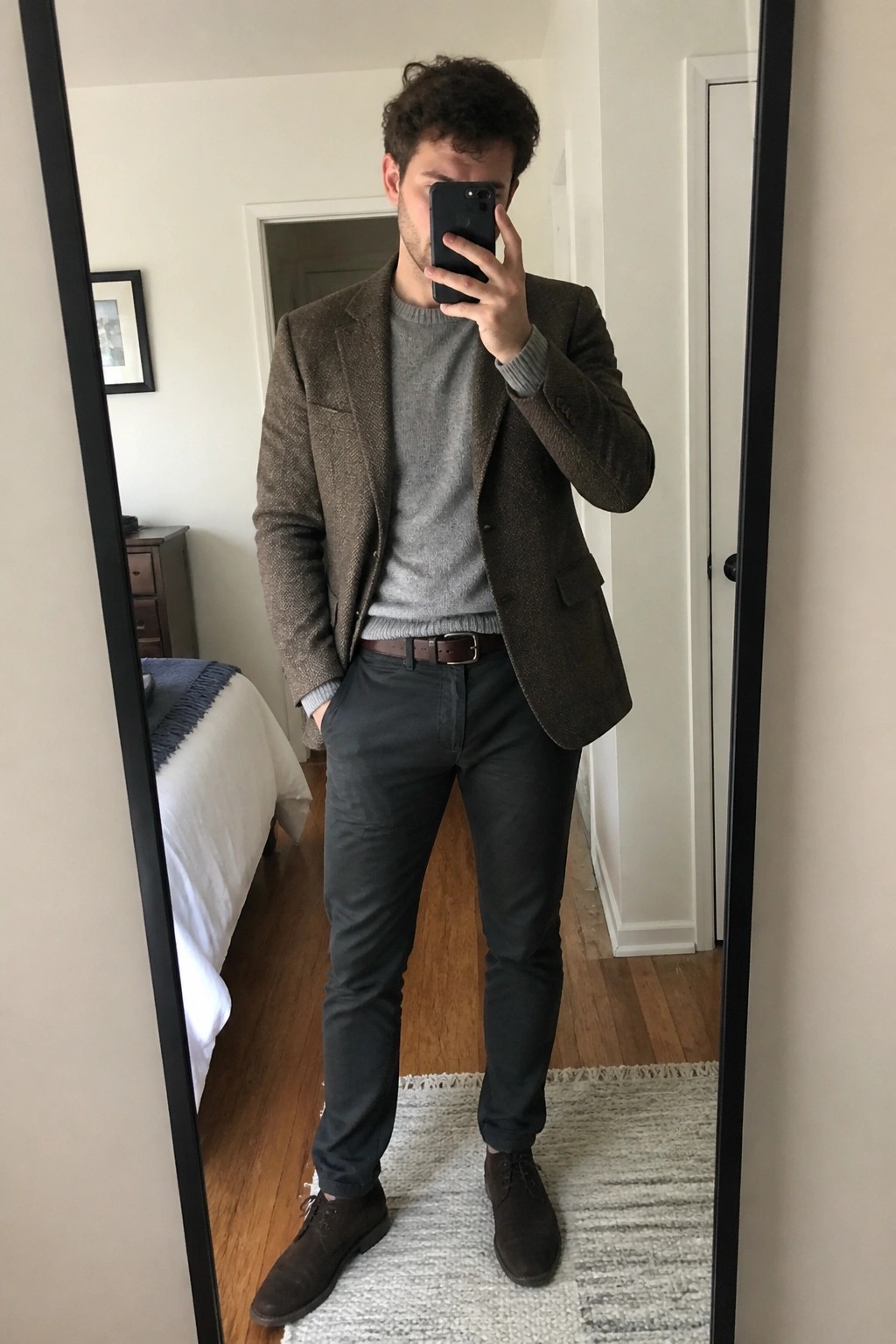 Man wearing brown tweed blazer over gray sweater with dark pants and brown shoes in mirror selfie.