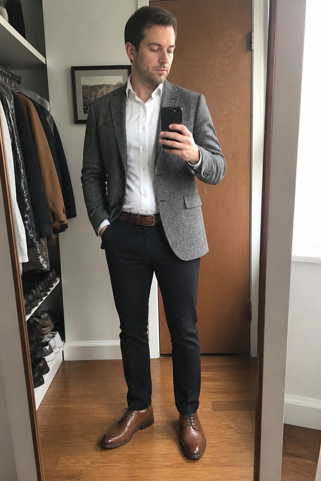 Man in gray blazer over white shirt taking mirror selfie in closet