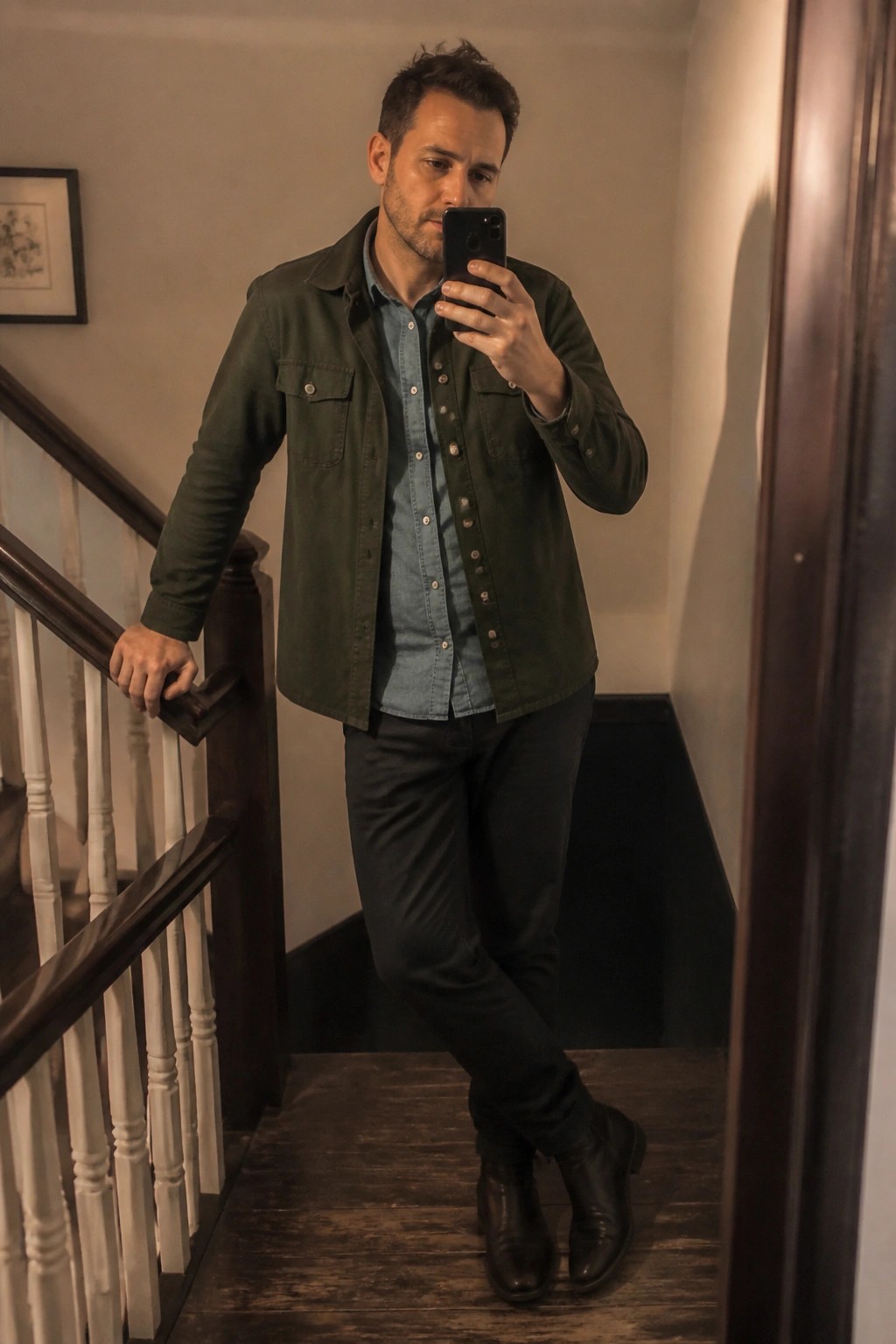 Man in green shirt takes selfie on wooden staircase wearing black boots.