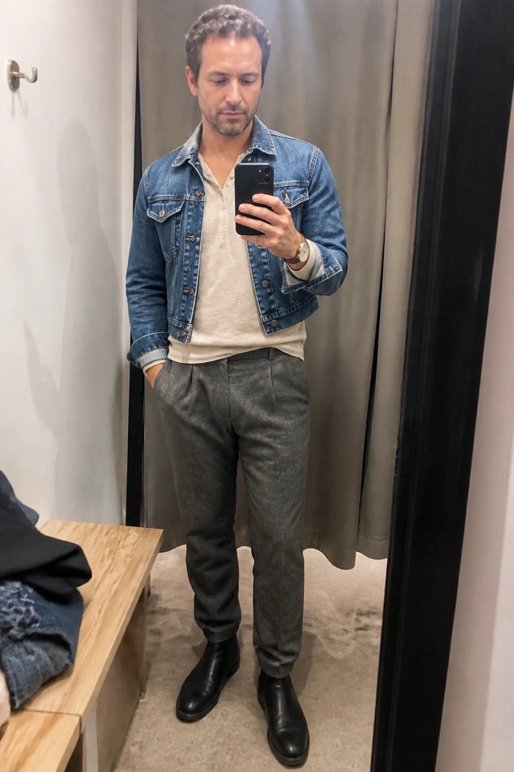 Man in blue denim jacket and gray pants taking mirror selfie with phone