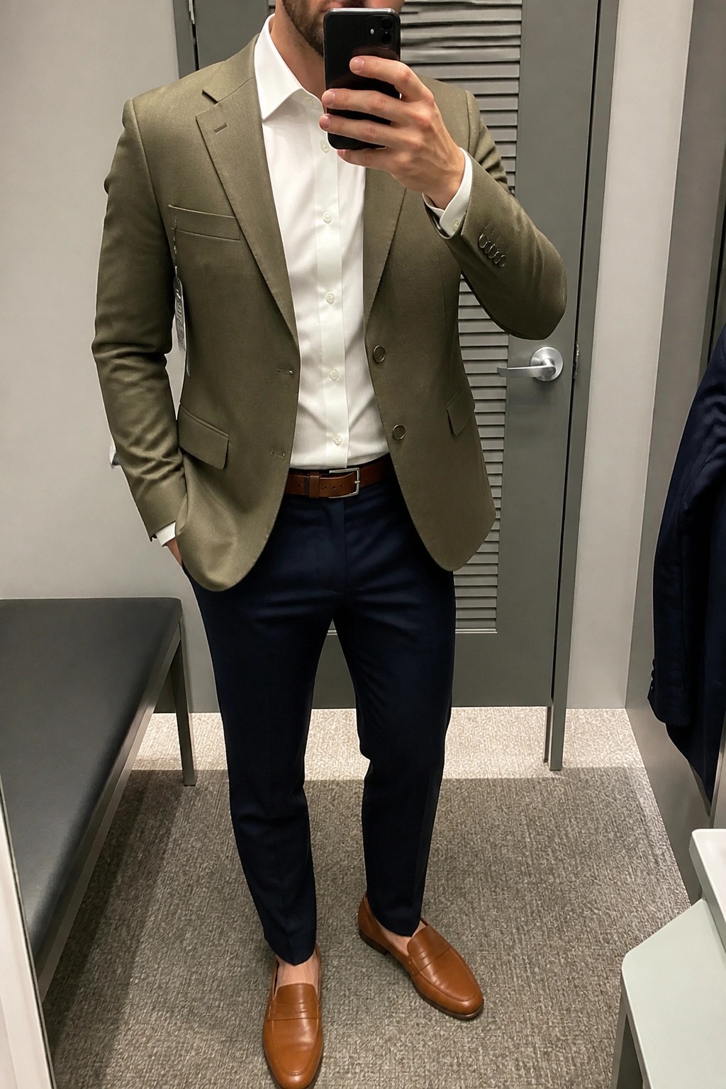 Man taking mirror selfie in olive blazer, white shirt, navy pants and brown loafers