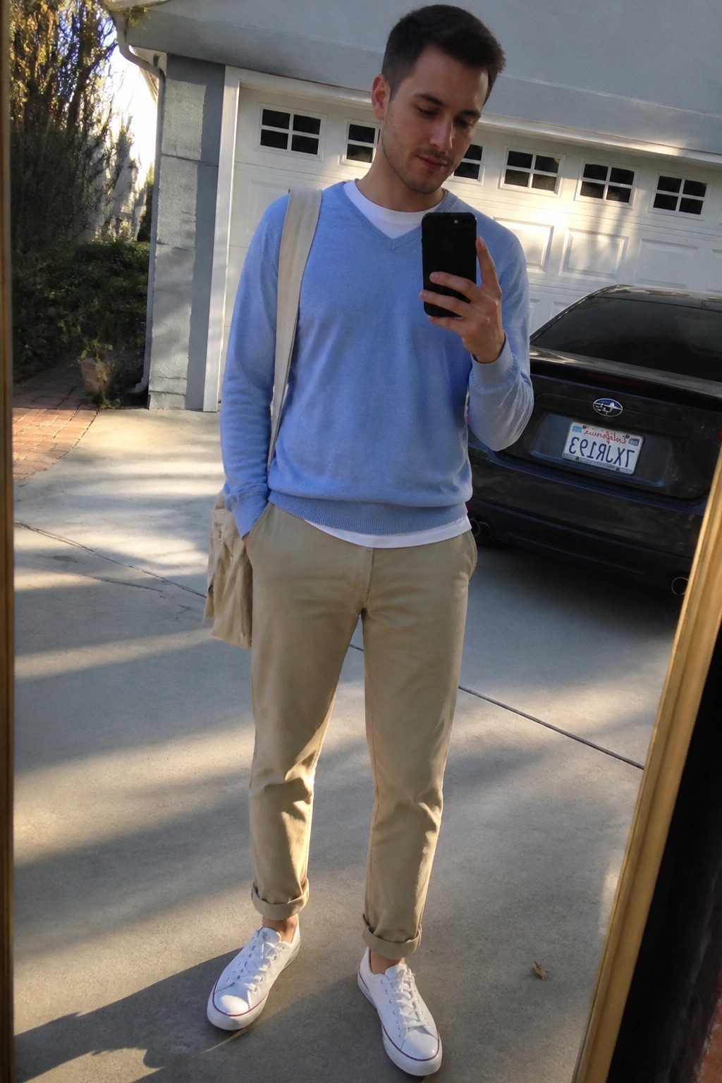 Man in light blue sweater and khaki pants taking mirror selfie with phone