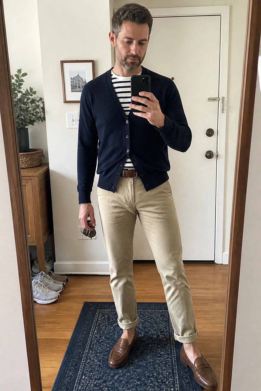 Man taking mirror selfie in navy cardigan, striped shirt, khaki pants, and loafers