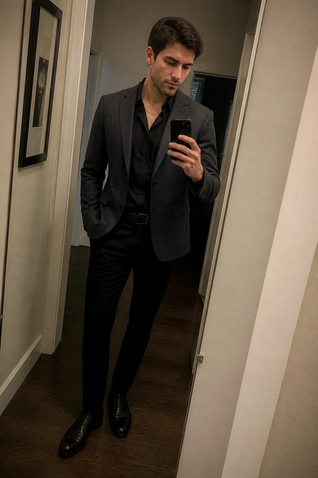 Man in gray blazer and black shirt taking mirror selfie with phone.