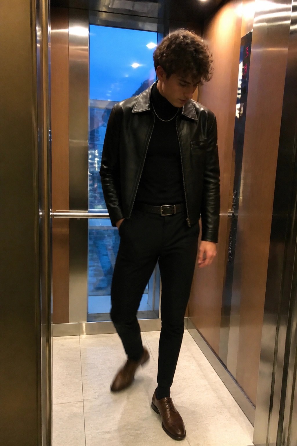 Young man in black leather jacket and turtleneck standing in elevator