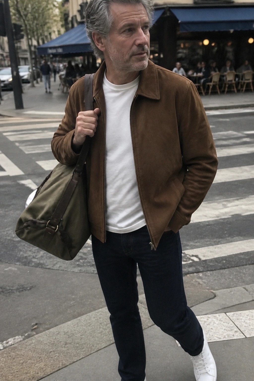 Man with graying hair in brown jacket carrying green canvas bag on city street