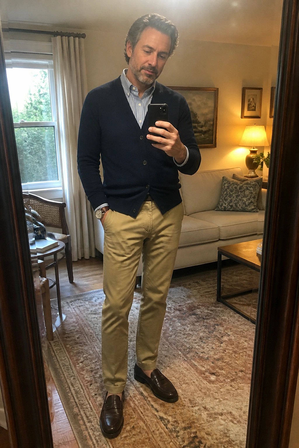 Man in navy cardigan and khaki pants taking mirror selfie in living room