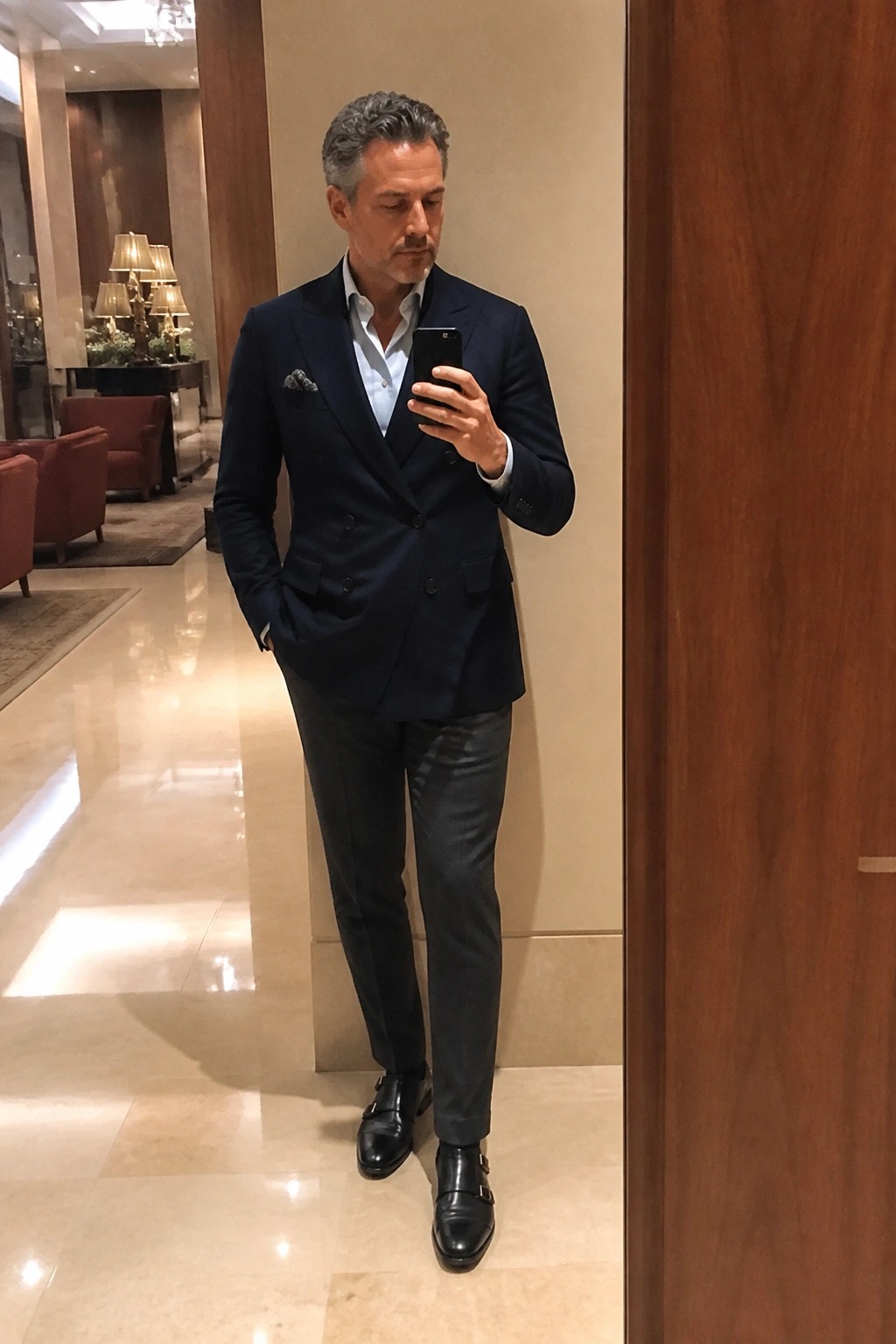 Man in navy double-breasted suit checks smartphone in elegant marble lobby