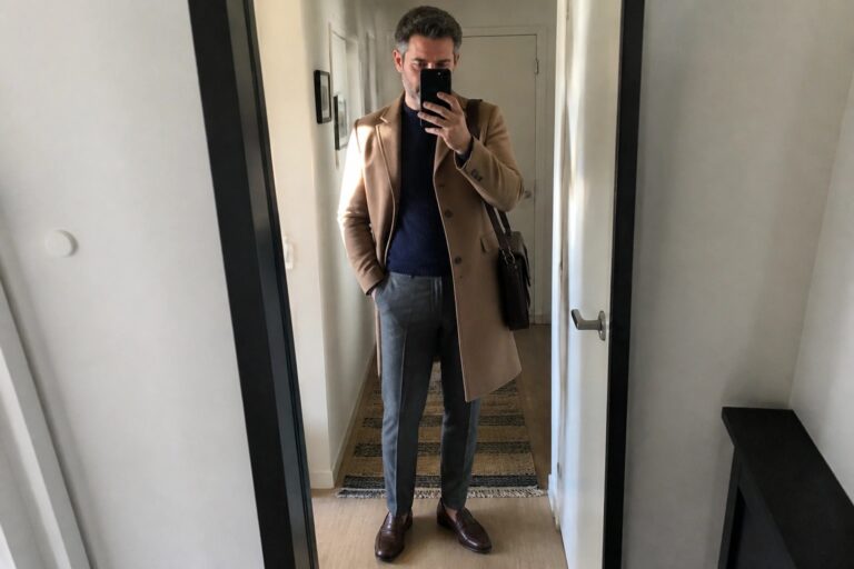 21 Stylish Old Money Fall Outfits for Men Over 40 Man in tan overcoat over navy sweater taking mirror selfie in hallway