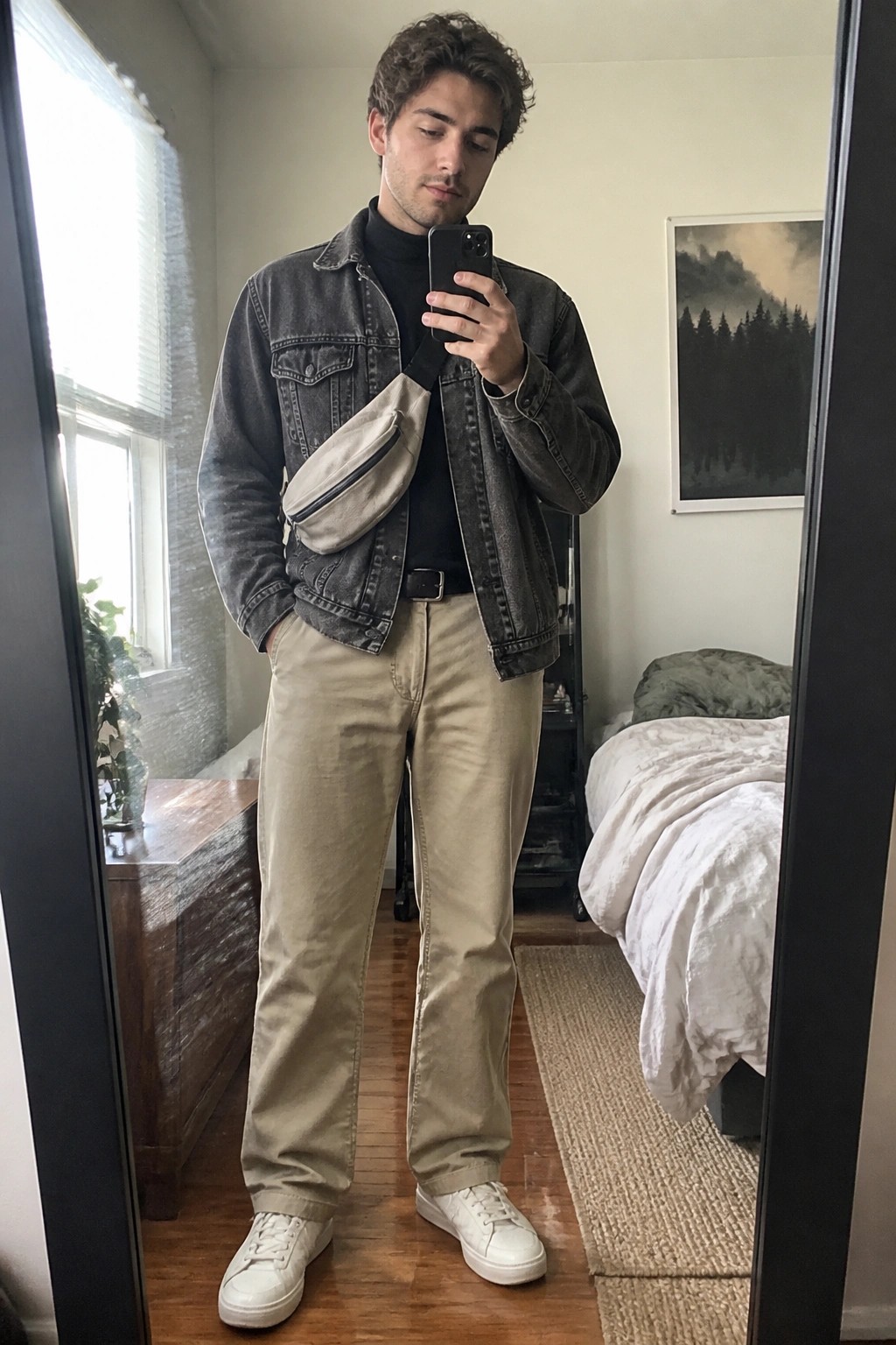 Young man in faded denim jacket and khaki pants taking mirror selfie with phone