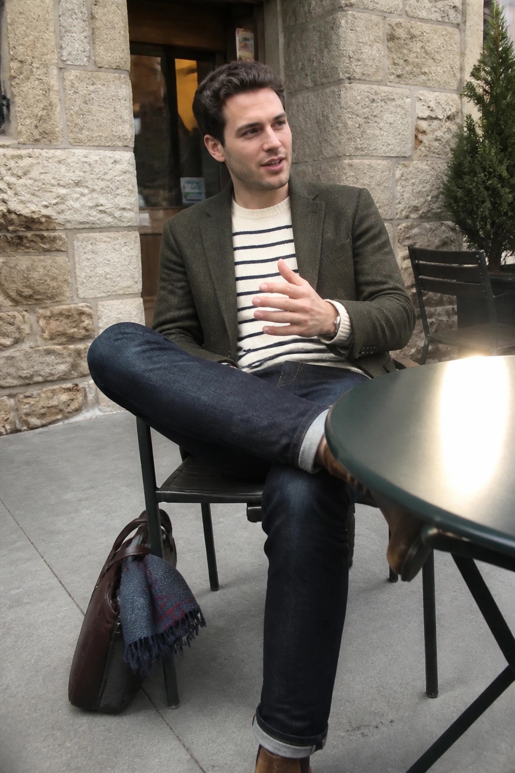 Man in green blazer and striped sweater gestures at outdoor cafe table