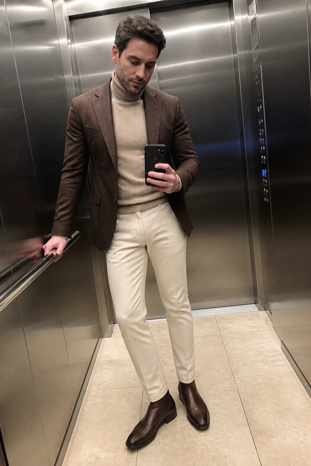 Man in brown blazer over beige turtleneck with cream pants in elevator