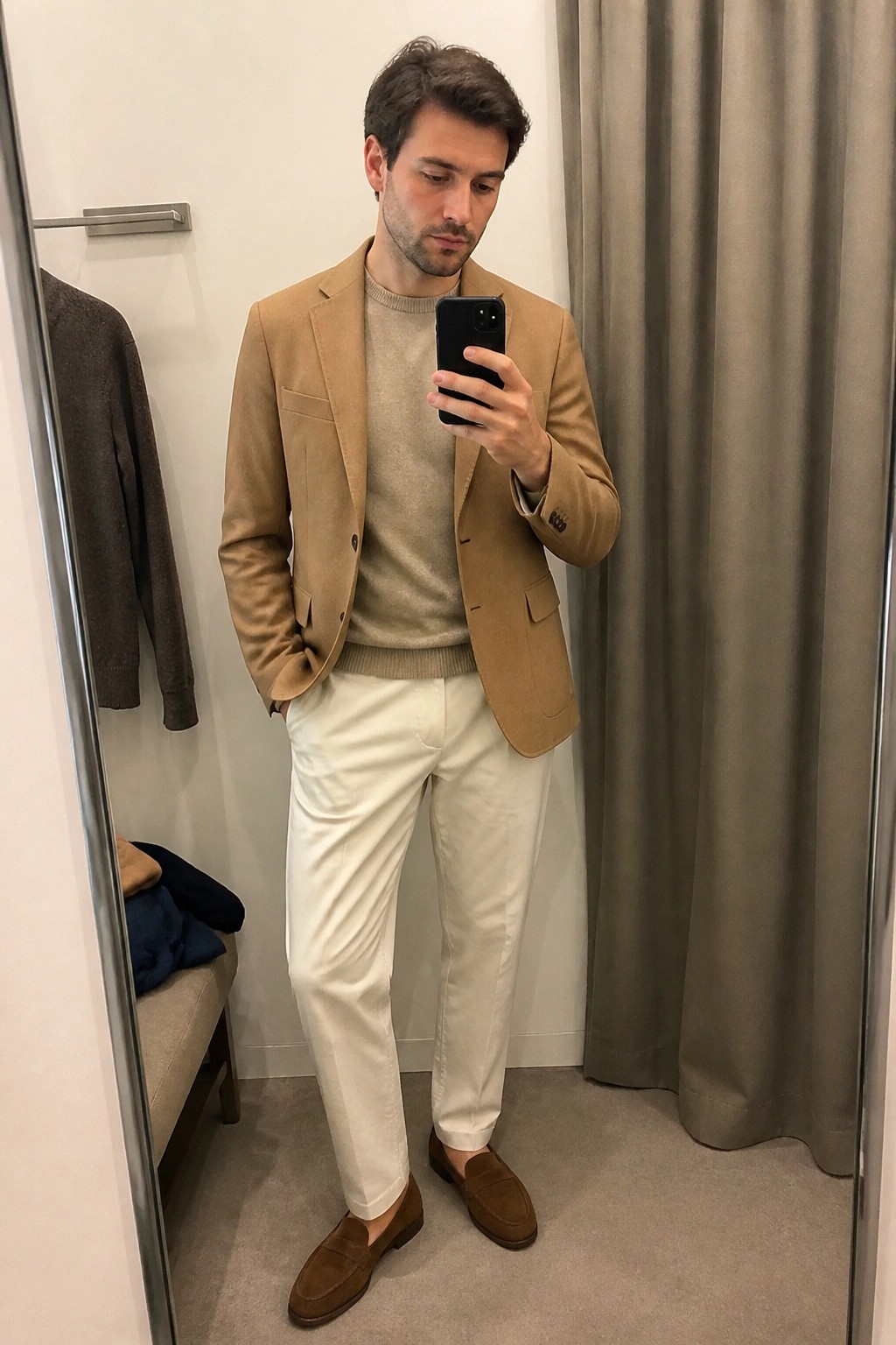 Man taking mirror selfie in tan blazer, beige sweater, white pants, and brown loafers