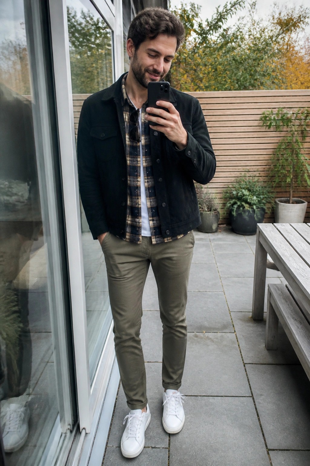Man in black jacket and plaid shirt checks smartphone on patio