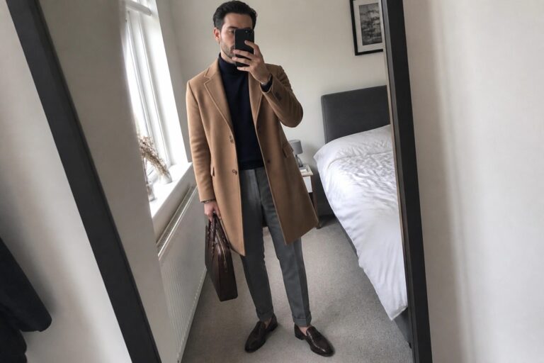 22 Sophisticated Old Money Fall Outfits for Men Featuring Wool Overcoats Man in tan overcoat over navy turtleneck holding briefcase during mirror selfie in bedroom.