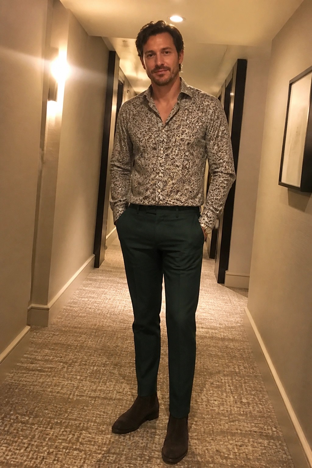 Man in patterned shirt and green pants standing in carpeted hallway