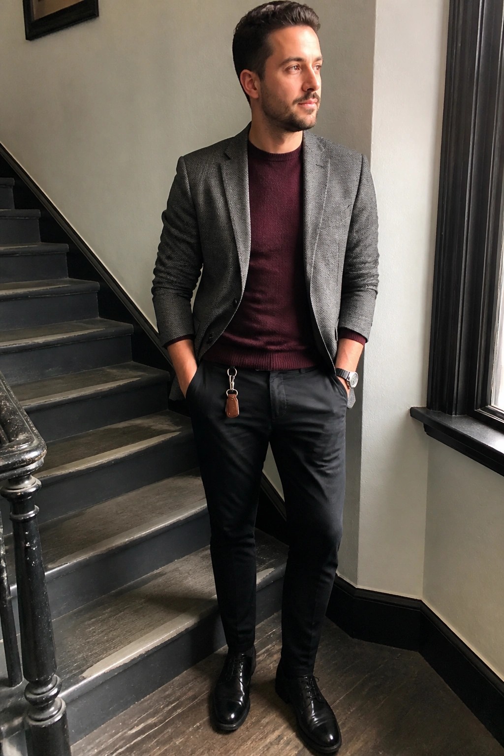 Man in gray blazer over maroon sweater with keychain on dark staircase.