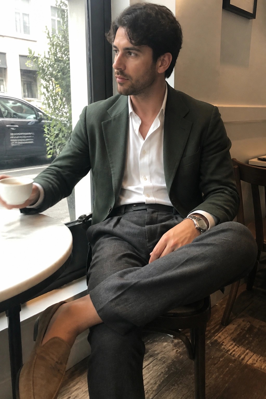 Man in green blazer holds coffee cup while seated by cafe window
