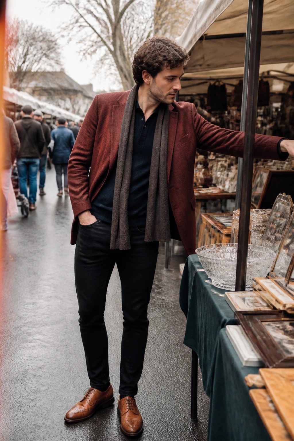 Man in maroon blazer and gray scarf at outdoor antique market stall with glassware