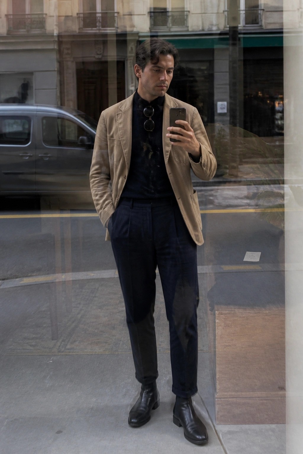 Man in tan blazer and navy trousers checks smartphone on city street