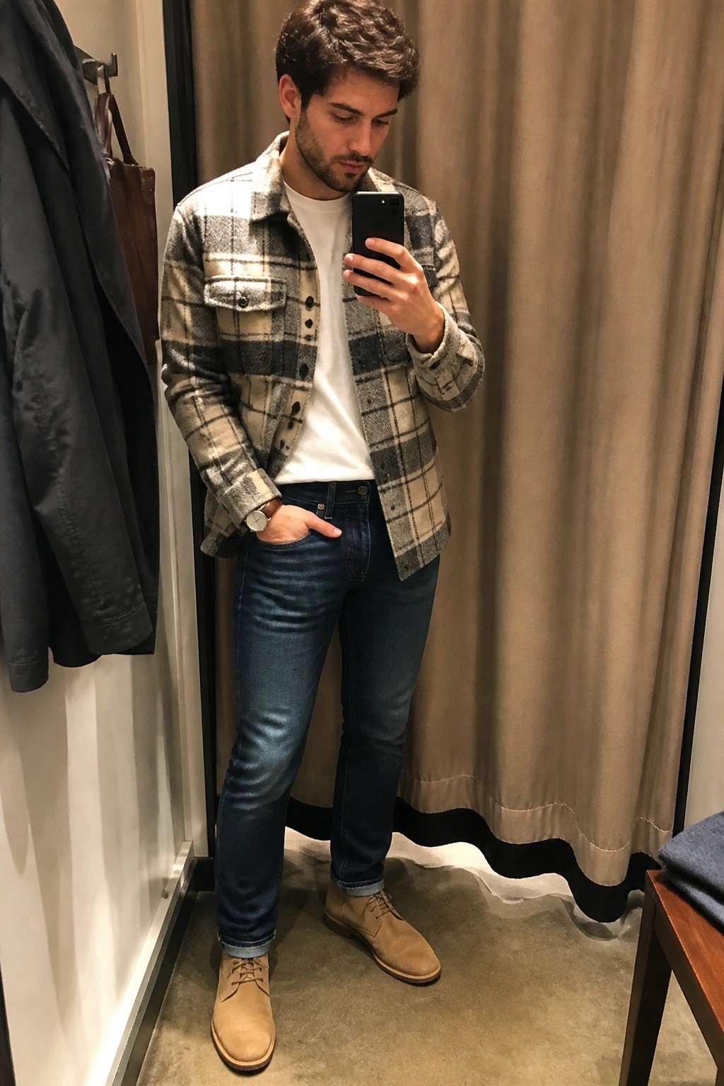 Man in plaid jacket and jeans taking mirror selfie in fitting room