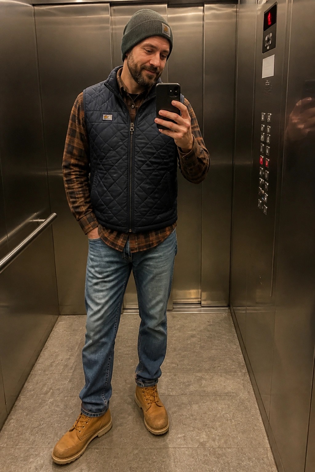 Bearded man in beanie and quilted vest takes mirror selfie in elevator