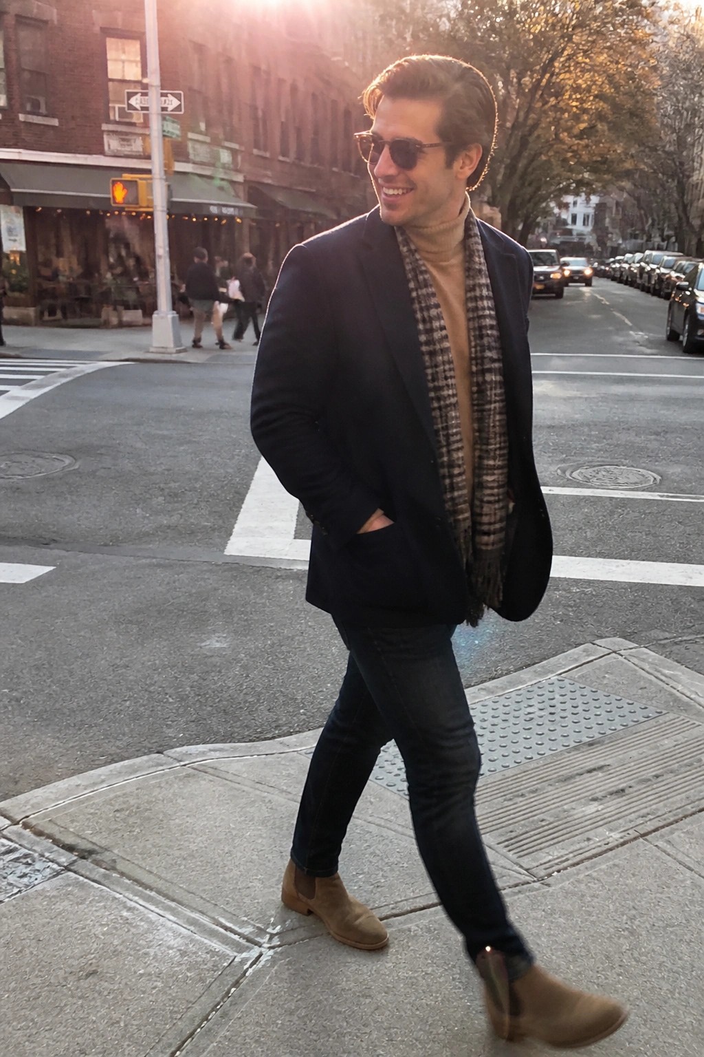 Man in navy blazer, turtleneck, and plaid scarf on sunny city street