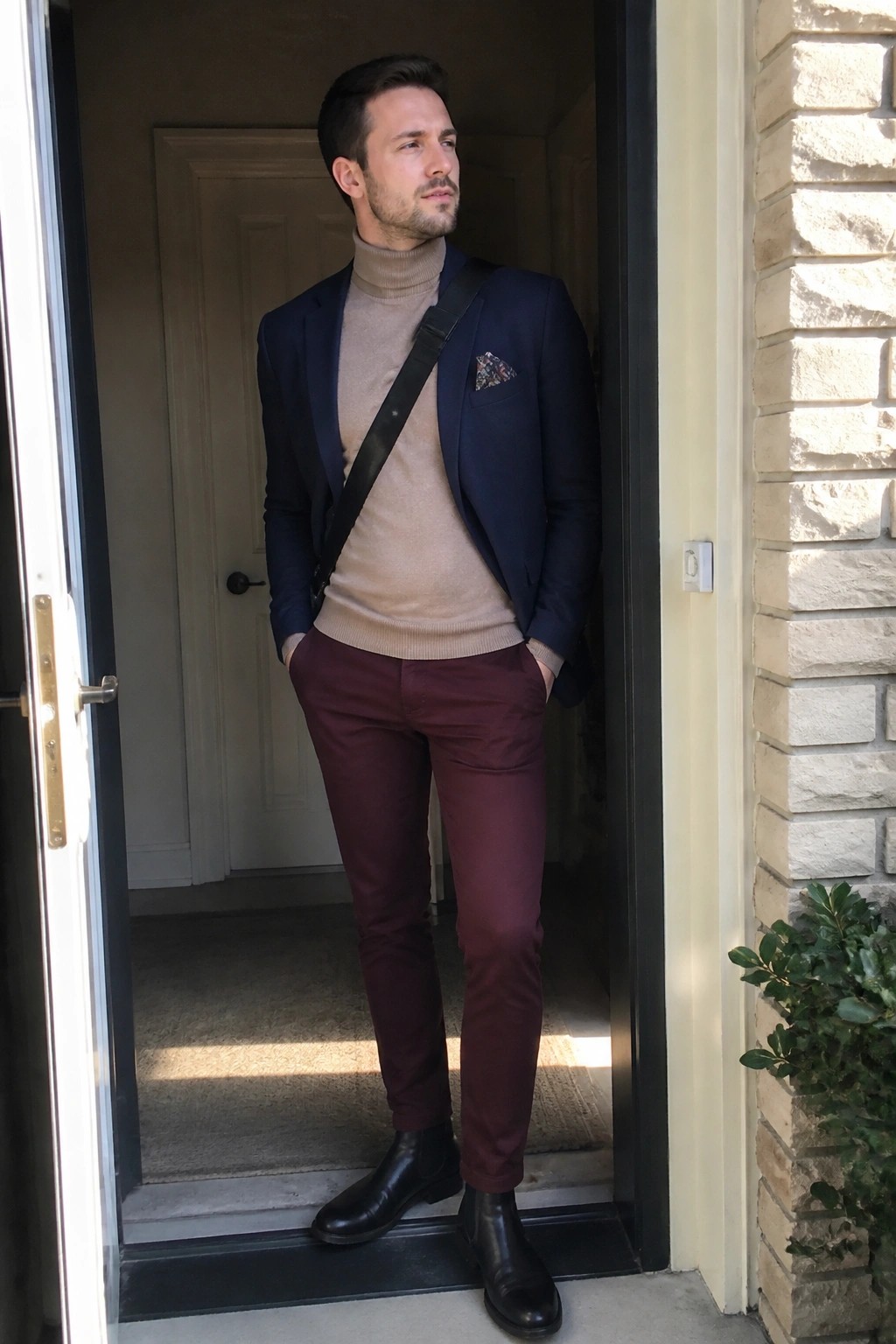 Man in navy blazer over beige turtleneck and maroon pants in doorway
