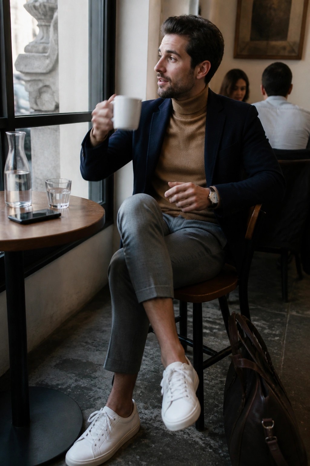 Man in navy blazer and tan turtleneck holding white mug at cafe table