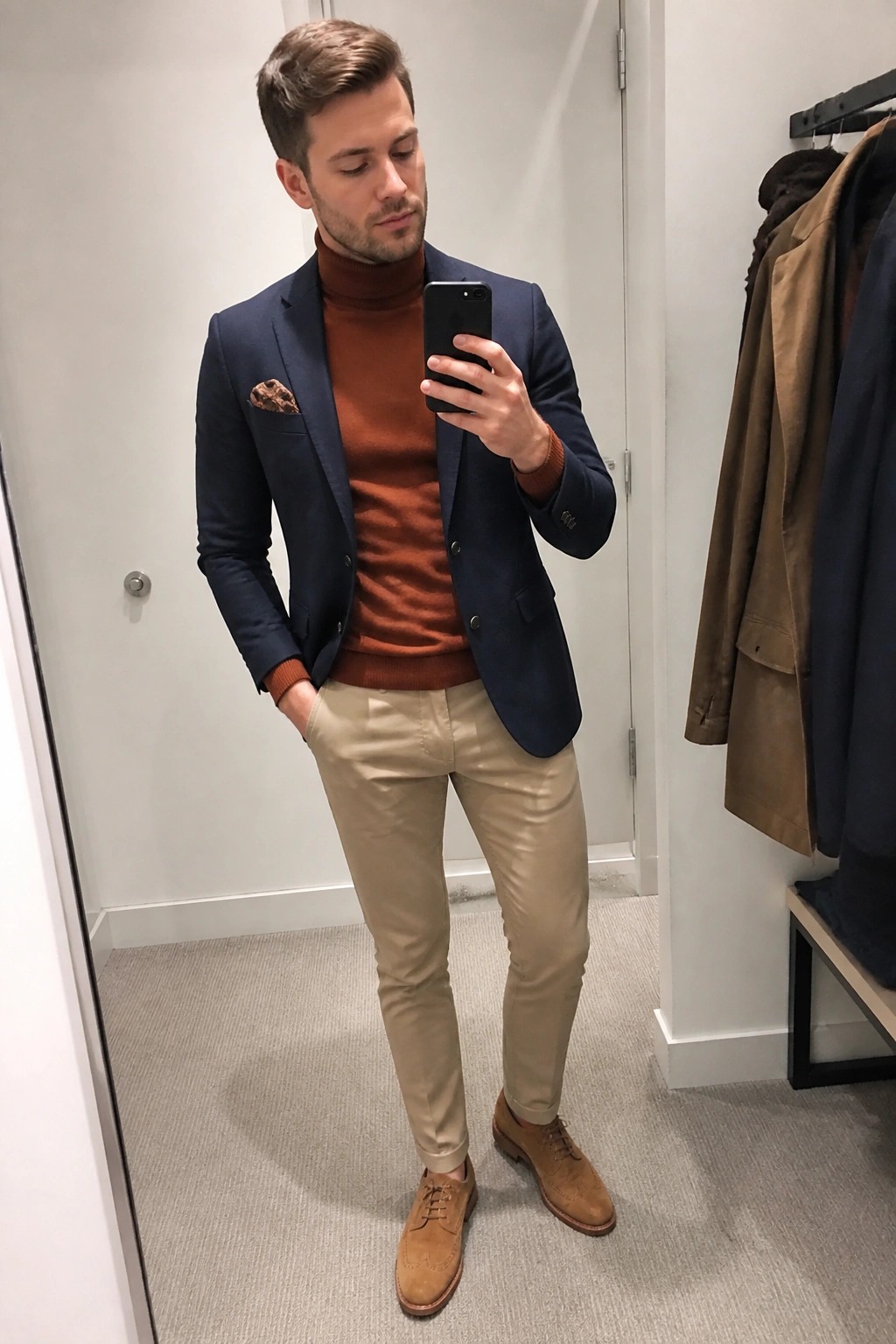Man in navy blazer over rust turtleneck and khaki pants taking mirror selfie