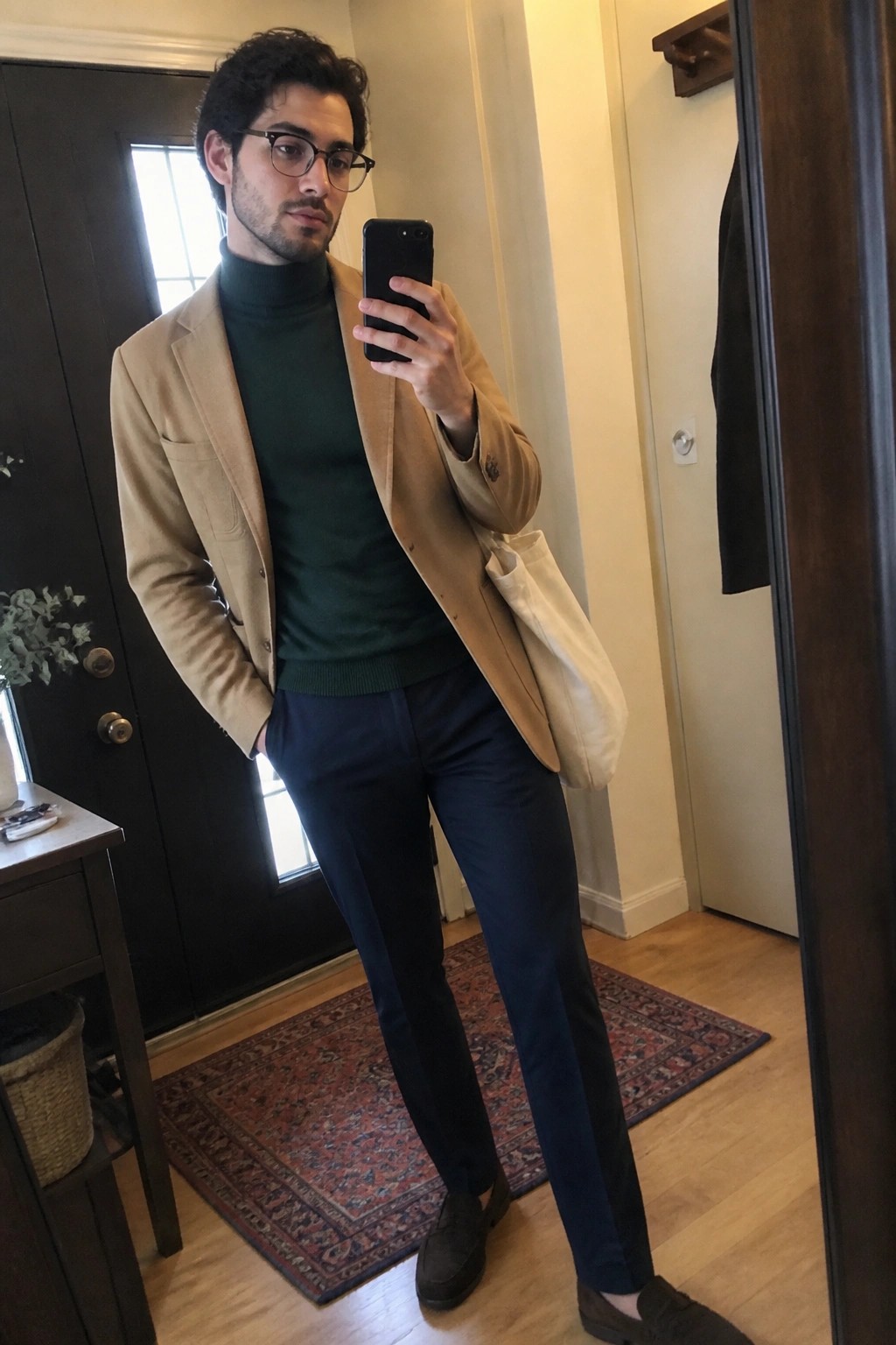 Man in tan blazer over green turtleneck taking mirror selfie with phone