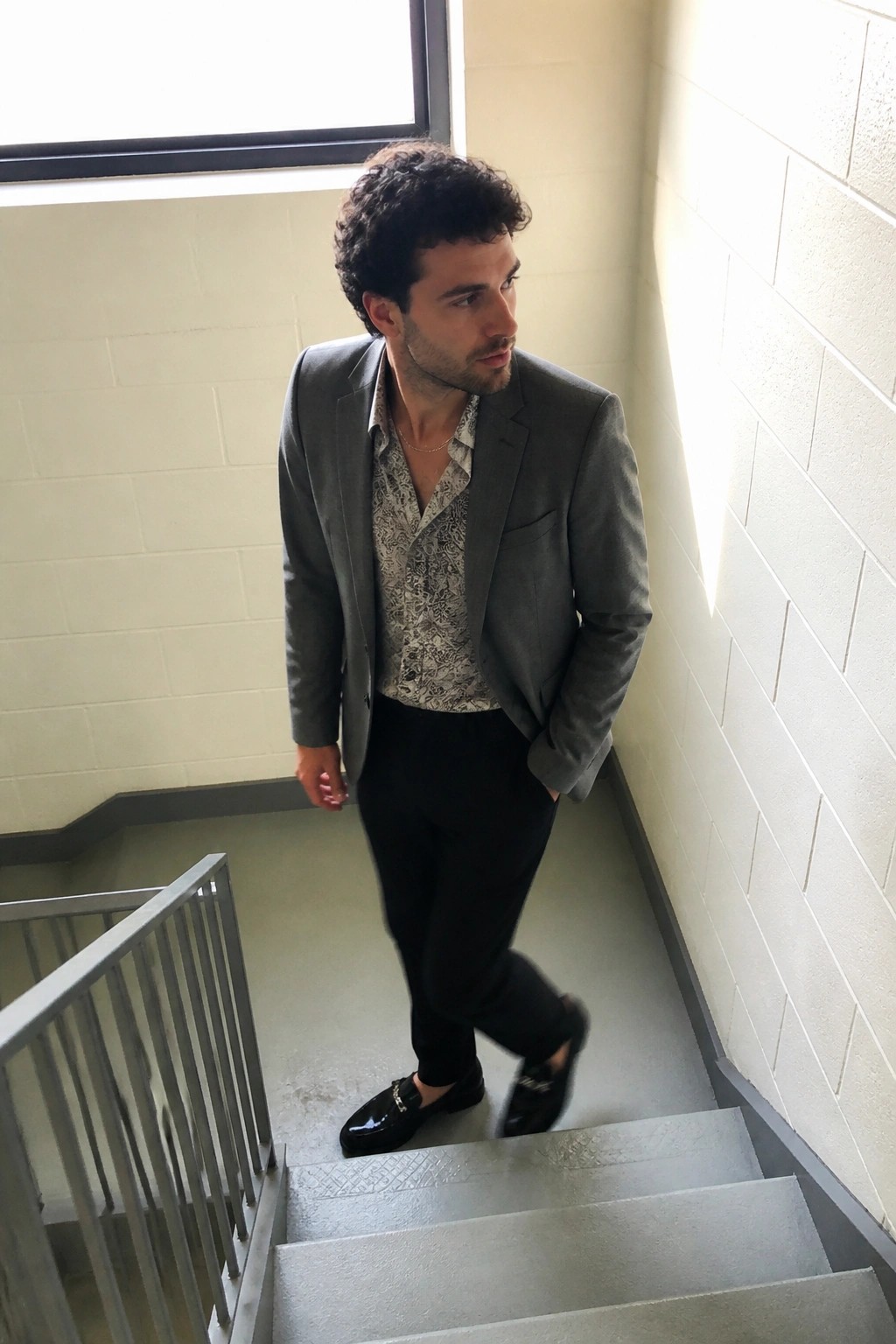 Man in gray blazer over patterned shirt on concrete stairwell steps
