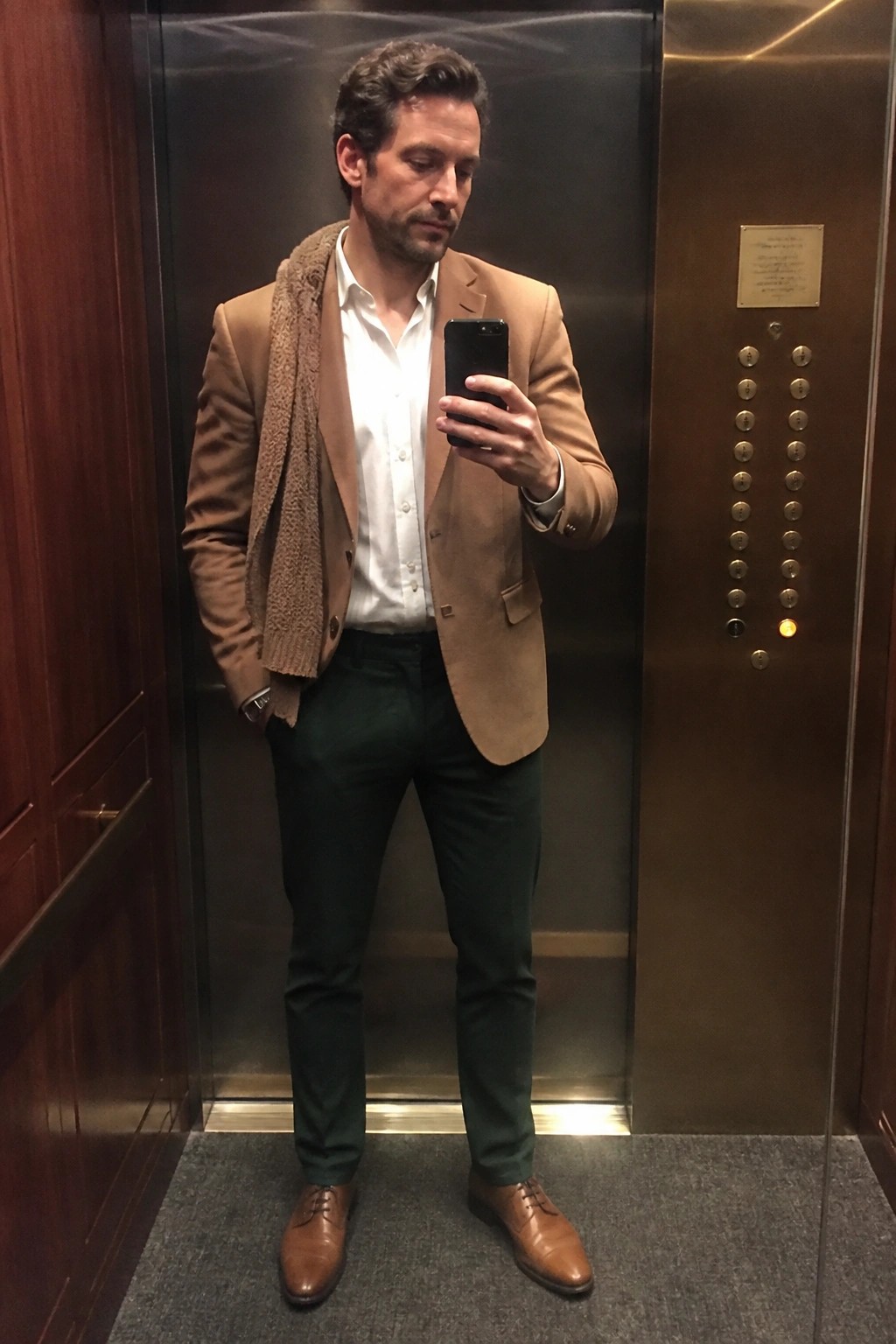 Man in tan blazer with brown scarf taking selfie in elevator