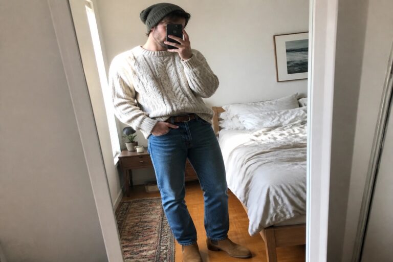 24 Cozy Men’s Fall Casual Outfits Featuring Chunky Sweaters and Straight-Leg Jeans Man in cream cable-knit sweater, blue jeans, brown beanie and boots taking mirror selfie.