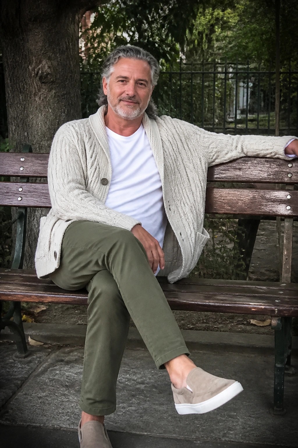 Gray-haired man in beige cardigan and olive pants seated on wooden park bench