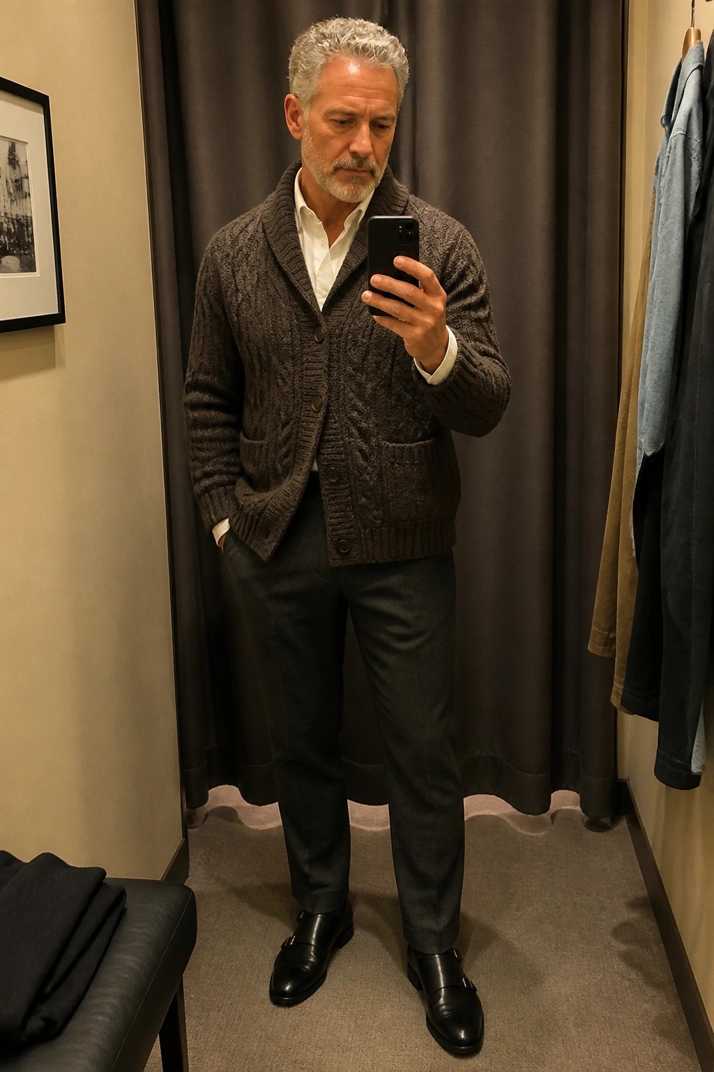 Gray-haired man in brown cardigan takes mirror selfie in fitting room.