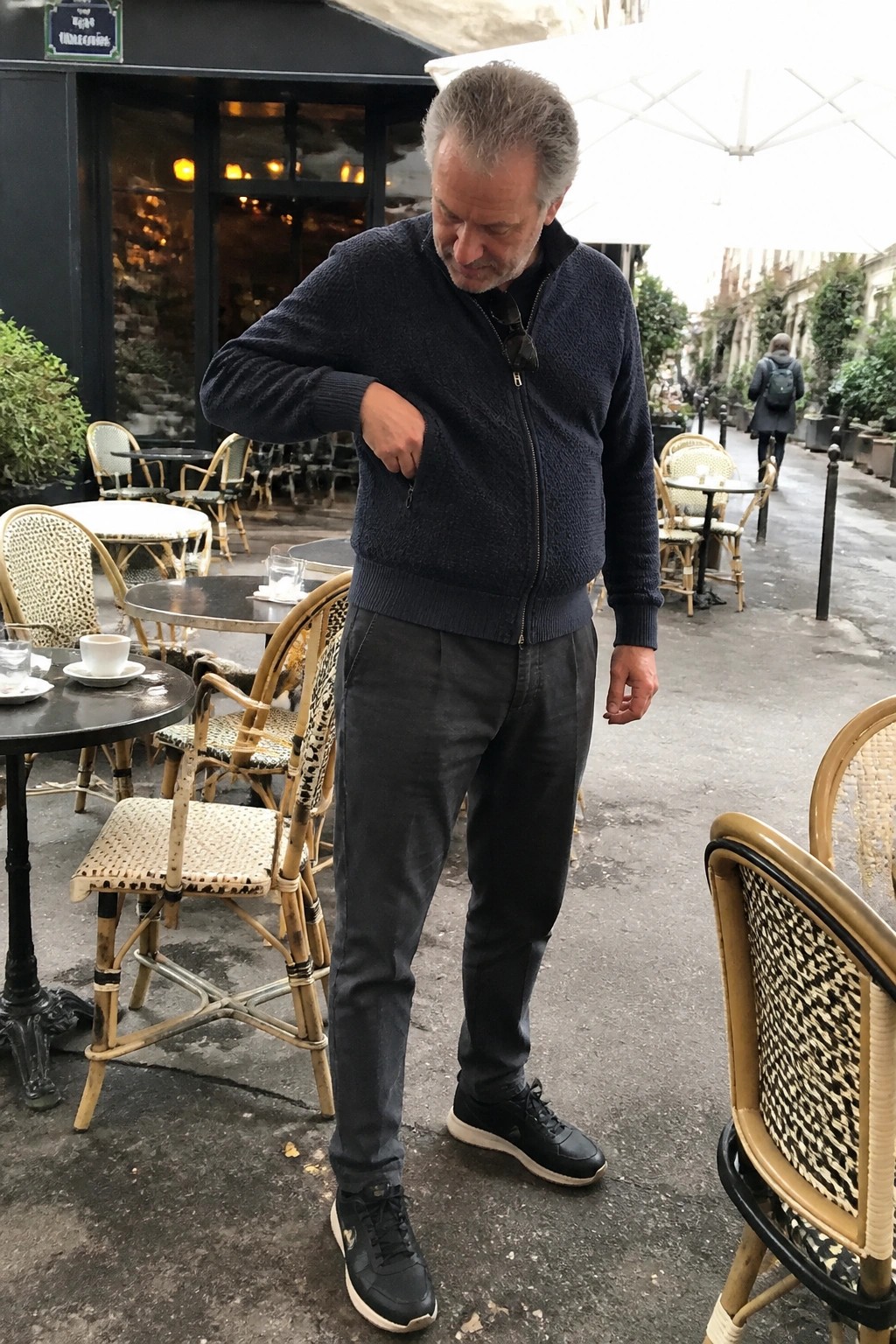 Man in navy zip sweater and gray pants at outdoor café patio
