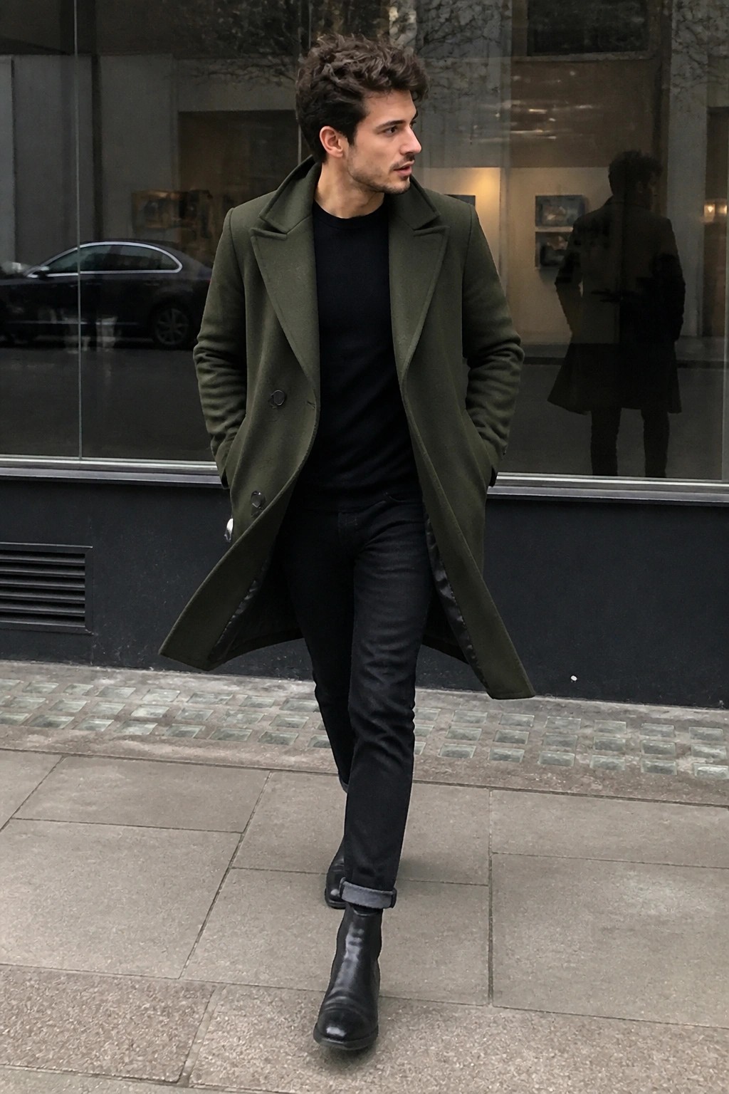 Man in olive green overcoat and black boots walking on city sidewalk
