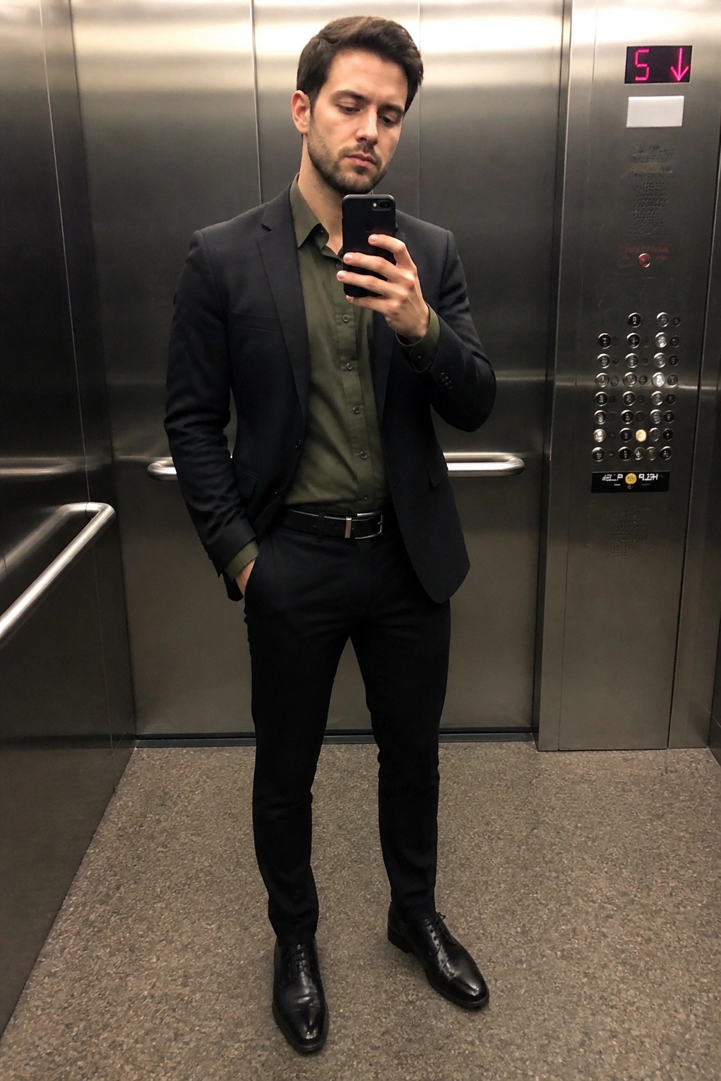 Man in black suit and green shirt taking selfie in elevator